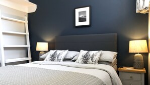 Une chambre à coucher comprenant un lit, deux tables de chevet, une commode, un tableau encadré accroché au mur et une étagère blanche.