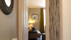Un couloir menant à une chambre à coucher équipée d’un lit, d’une table de chevet et d’une lampe.