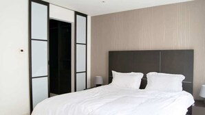 Quarto moderno com uma cama grande, cabeceira escura e um guarda-roupa com portas de correr.