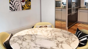 Uma sala de jantar com uma mesa de mármore, cadeiras verdes e uma cozinha moderna ao fundo.