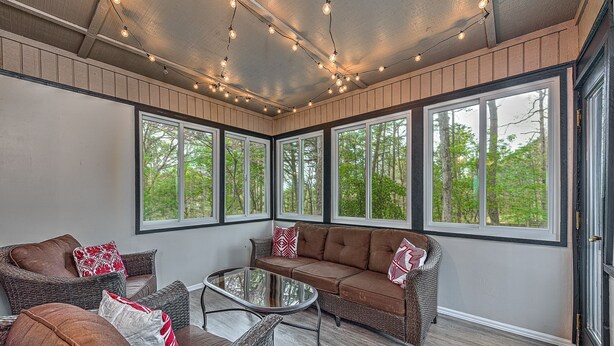 A sunroom with wicker furniture, large windows, and string lights. - Mountain Bikers Retreat (Bella Vista)