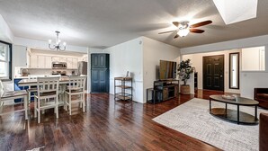 A spacious living area with hardwood flooring, a dining set, a ceiling fan, and a kitchen in the background. - Mountain Bikers Retreat (Bella Vista)
