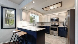 A modern kitchen with white cabinets, a central island, stainless steel appliances, and a large window. - Mountain Bikers Retreat (Bella Vista)