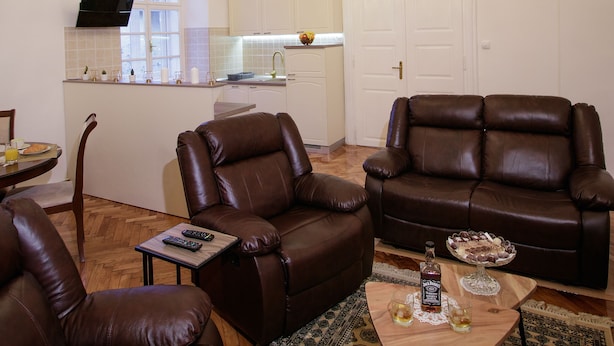 Een woonkamer met twee bruine leren banken, een houten salontafel, een kamerkleed met patroon en een kroonluchter.