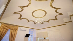 Een kamer met een decoratief plafond, een kroonluchter, een raam met gordijnen en een wastafel.