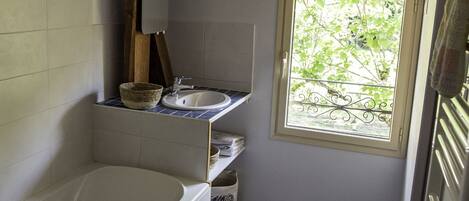 Une salle de bain avec une baignoire, une fenêtre donnant sur un paysage verdoyant et des carreaux de sol à motifs.