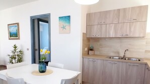 A modern kitchen with light wood cabinets, a stainless steel sink, and a dining area with a white table and chairs. - Casa Maria (Tanaunella)