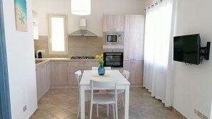 A modern kitchen with white cabinets, a gas stove, an oven, a microwave, and a dining table with chairs. - Casa Maria (Tanaunella)