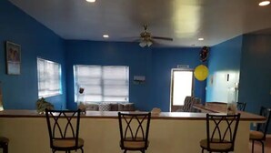 A bar area with three stools, a ceiling fan, and a door labeled "ENTRADA". - Delancy's Cottage (north caicos)