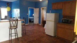 A kitchen with blue walls, a refrigerator, and wooden cabinets. - Delancy's Cottage (north caicos)