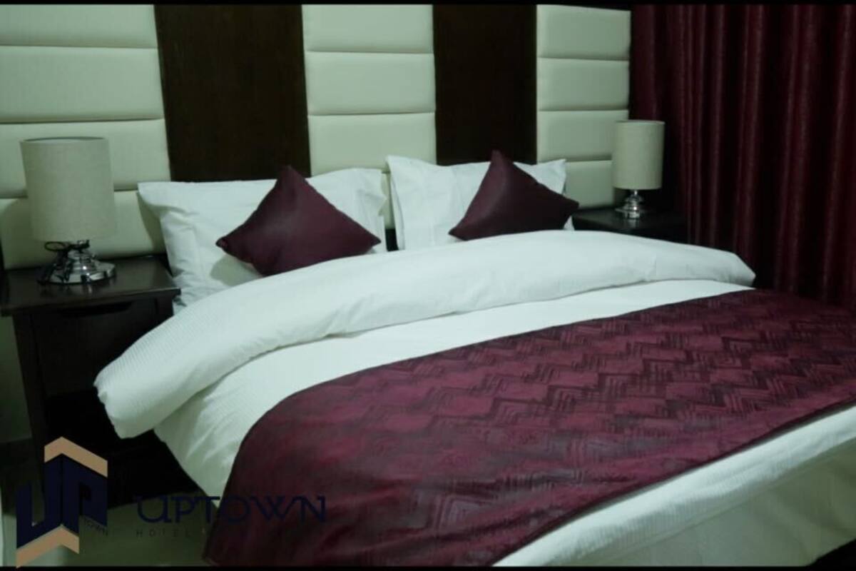 A hotel room with a large bed, two nightstands, a headboard, and a red curtain.