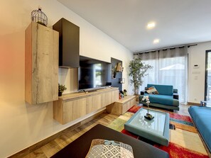 Un salon moderne avec un téléviseur à écran plat, des meubles en bois, un canapé bleu et une table basse en verre.