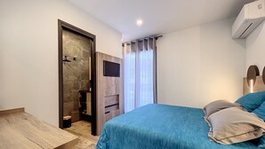 A bedroom with a bed, a TV mounted on the wall, a wooden desk, and a shower area. - Villas A du Golf Mougins (Mougins)