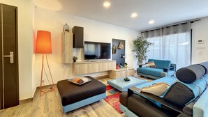 A modern living room with a sofa, ottoman, and a flat-screen TV. - Villas A du Golf Mougins (Mougins)