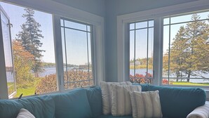 Un canapé d’angle de couleur turquoise agrémenté de coussins à rayures, une table basse en bois et de grandes fenêtres offrant une vue sur un lac et des arbres.