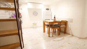 A clean, modern kitchen with white cabinets, a wooden dining table, and chairs. There is a microwave on the wall, a trash can, and a clock. - Casa Opera lovely apartment in Rome (Roma)