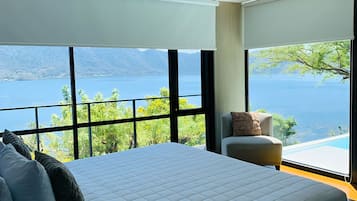 A bedroom with a large bed, a chair, and a view of a lake and mountains.