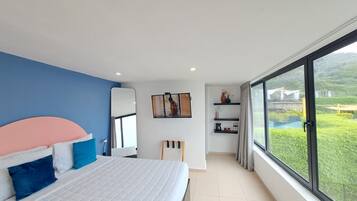 A modern bedroom with a large bed, a TV, and a view of a green landscape through a large window.