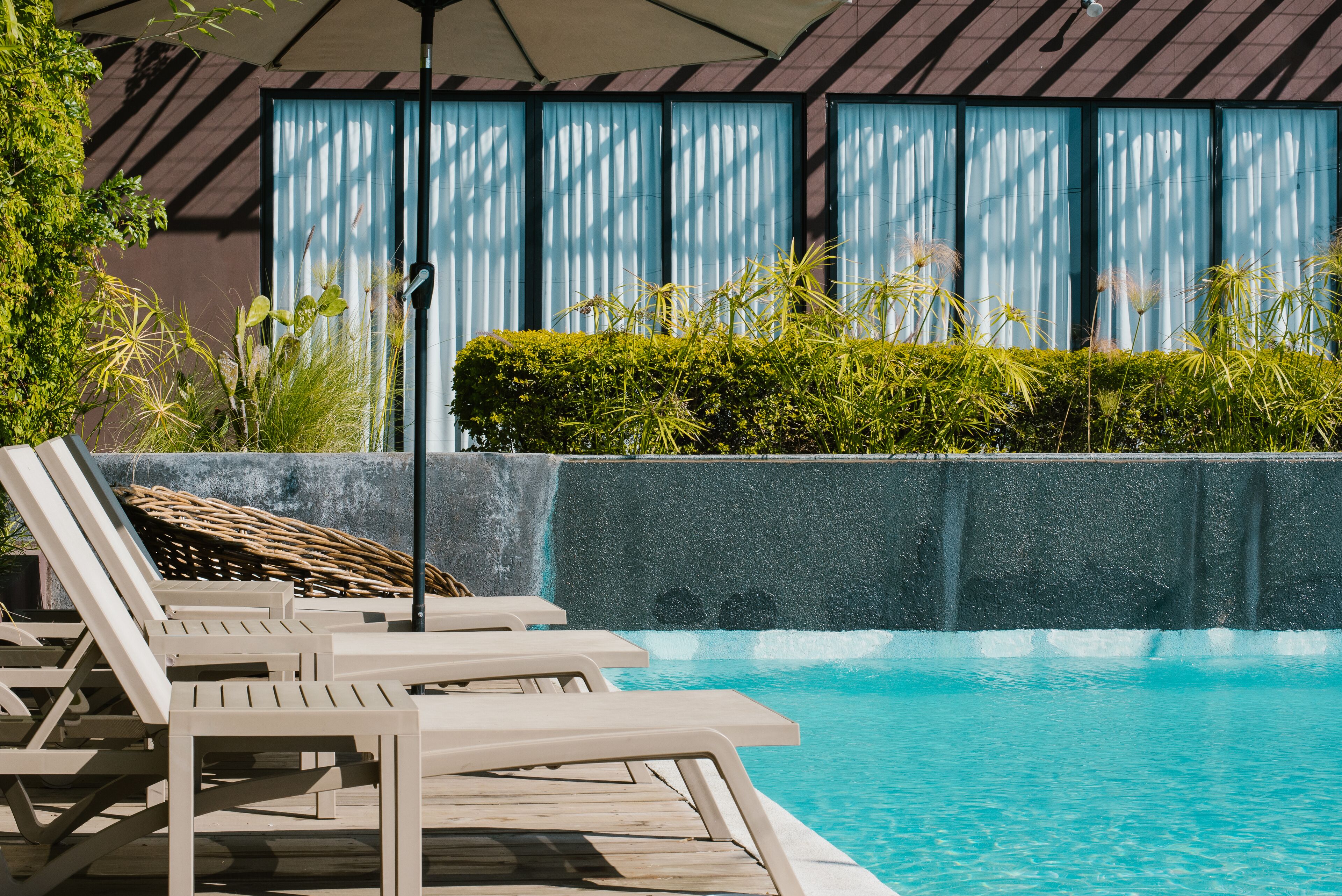 A pool area with lounge chairs, a waterfall feature, and a view of a building with large windows.