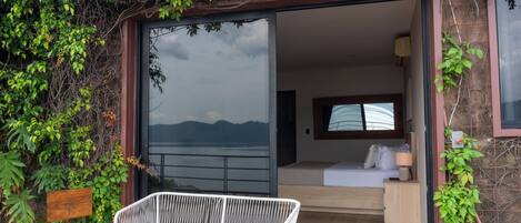 A room with a bed, a bedside table, and a window with a view of the sea.