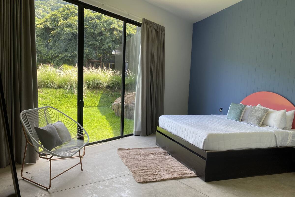 A bedroom with a bed, a chair, and a view of a garden through a sliding door.