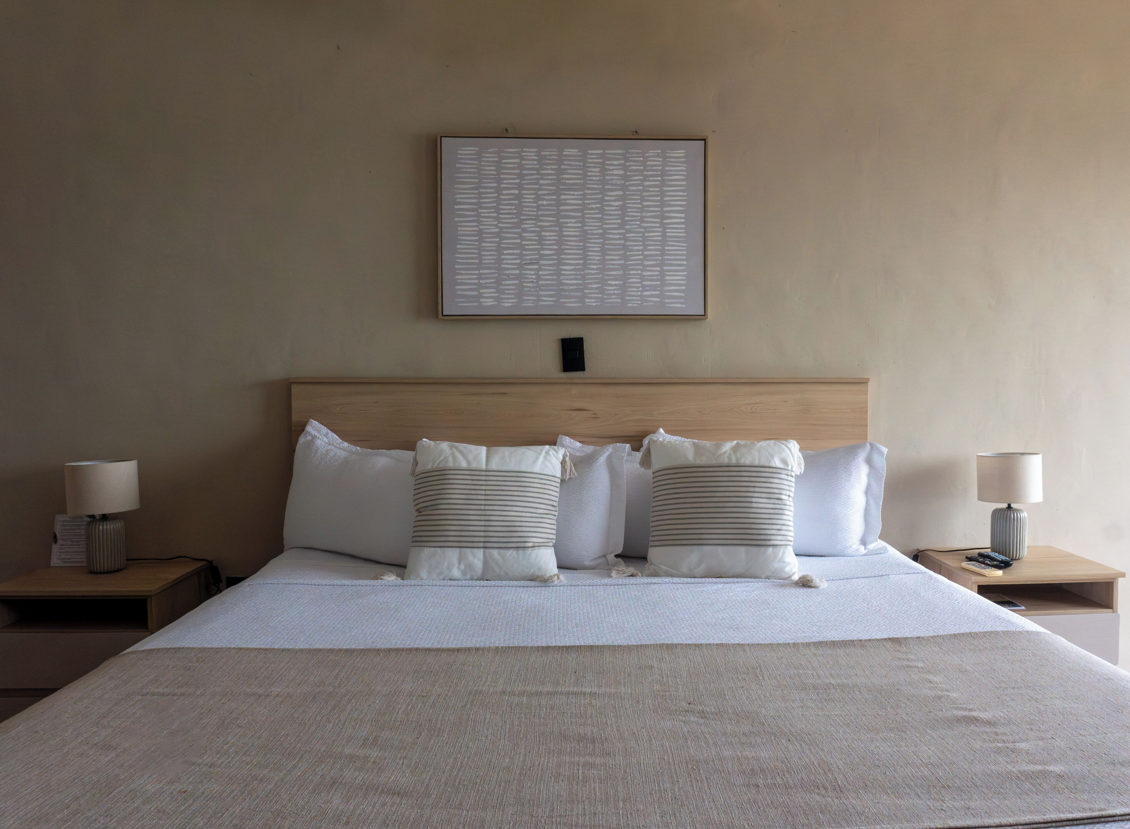 A neatly made bed with a headboard, two bedside tables with lamps, and a framed picture on the wall.