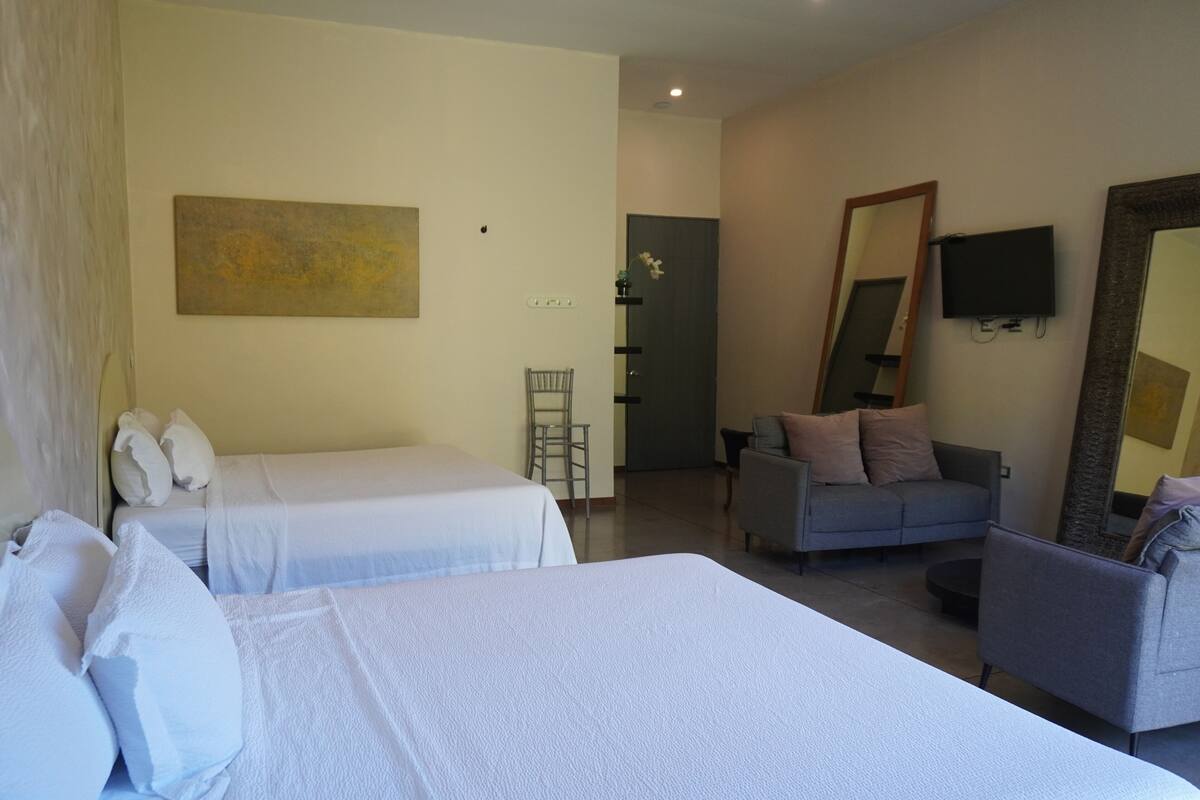 A hotel room with two beds, a sofa, a chair, a TV, and a large mirror.
