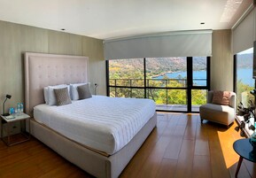 Un dormitorio con una cama grande, una mesita de noche, una silla y vistas a un lago y montañas.