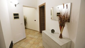 Een hal met een lichtgekleurde betegelde vloer, een receptiebalie met een vaas, een spiegel en een deur naar een andere kamer.