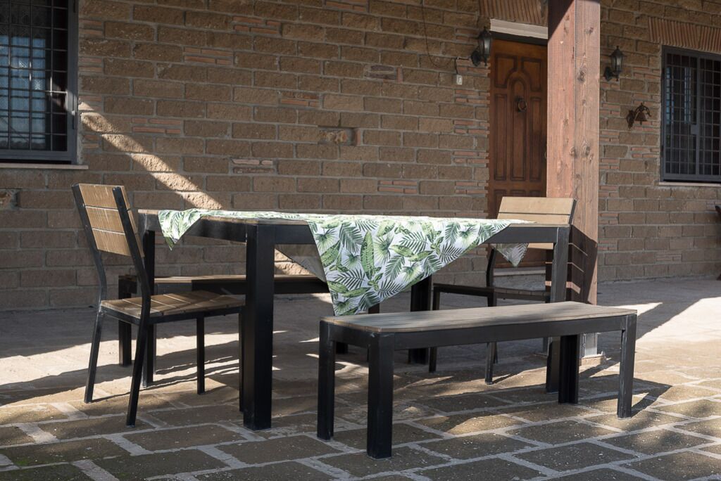 Un espace extérieur aménagé avec une table et des chaises, un banc, et un bâtiment en briques en arrière-plan.