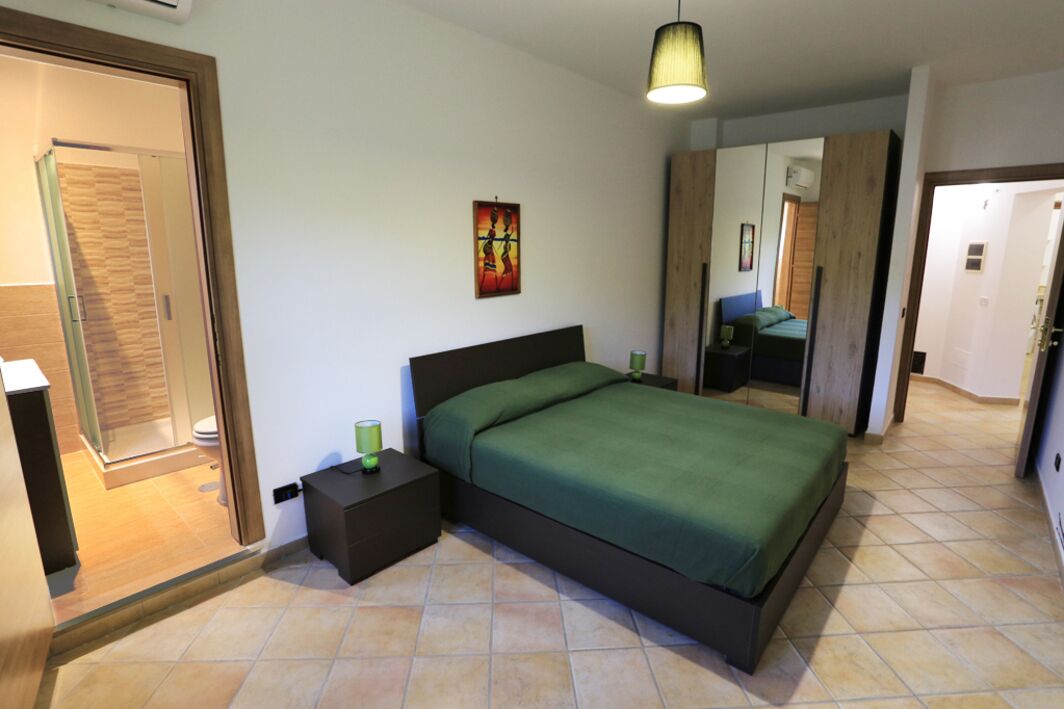 Een slaapkamer met een bed, nachtkastjes, een hanglamp en een deur naar een badkamer.