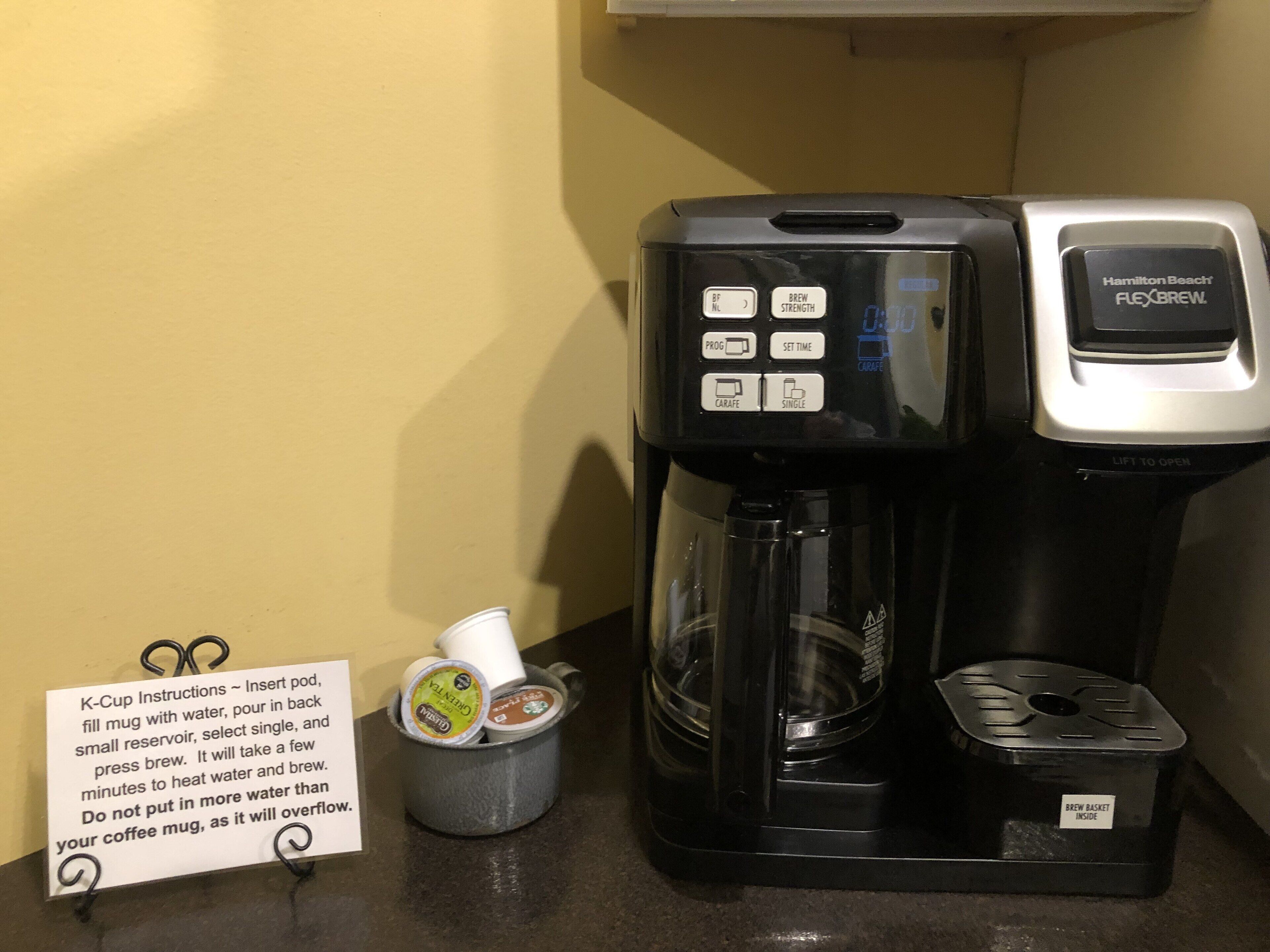 A Hamilton Beach Flexbrew coffee maker with a drip tray and a brew basket, a K-Cup pod holder, and a coffee mug.