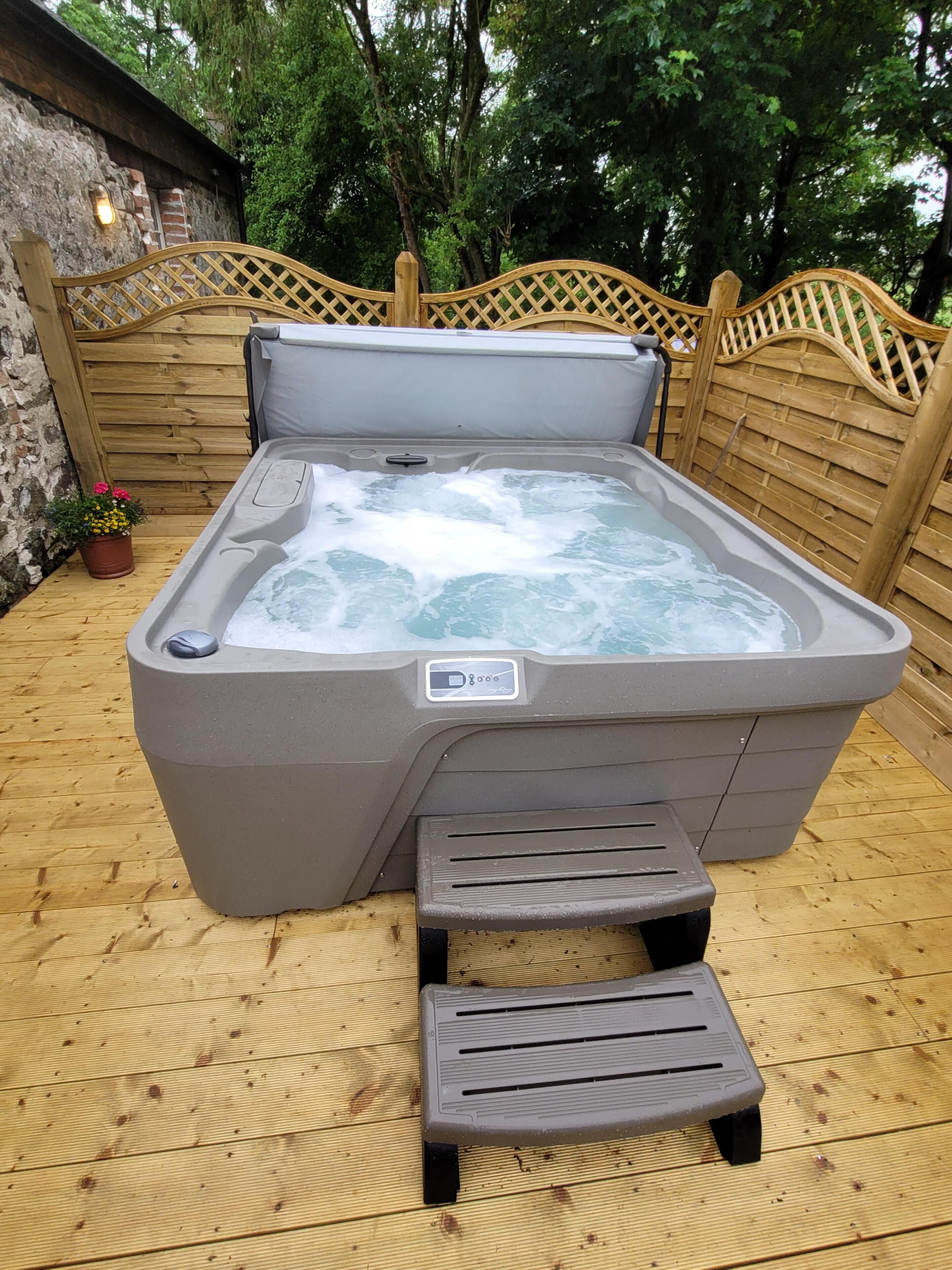 A hot tub with a control panel, a wooden deck, and a wooden fence.