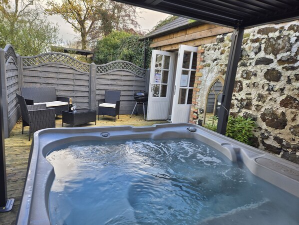 A hot tub in a backyard with a wooden fence, a table with chairs, and a stone wall. - Hawthorn Hollow (Ballymena)