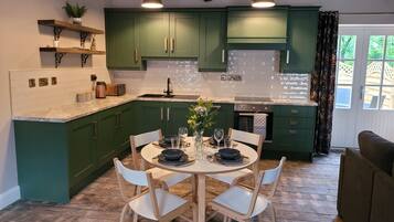 A kitchen with green cabinets, a dining table with chairs, and pendant lights.