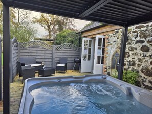 A hot tub with a wooden deck, a covered seating area, and a stone wall. - Hawthorn Hollow (Ballymena)