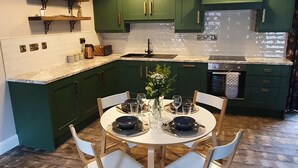 A kitchen with green cabinets, a round dining table with chairs, and pendant lights. - Hawthorn Hollow (Ballymena)