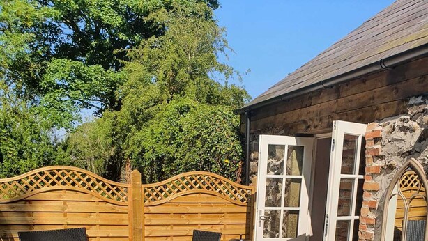 A hot tub in a backyard with wooden chairs and a stone wall. - Hawthorn Hollow (Ballymena)