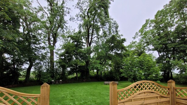 A wooden deck with a view of a lush green lawn and trees. - Hawthorn Hollow (Ballymena)