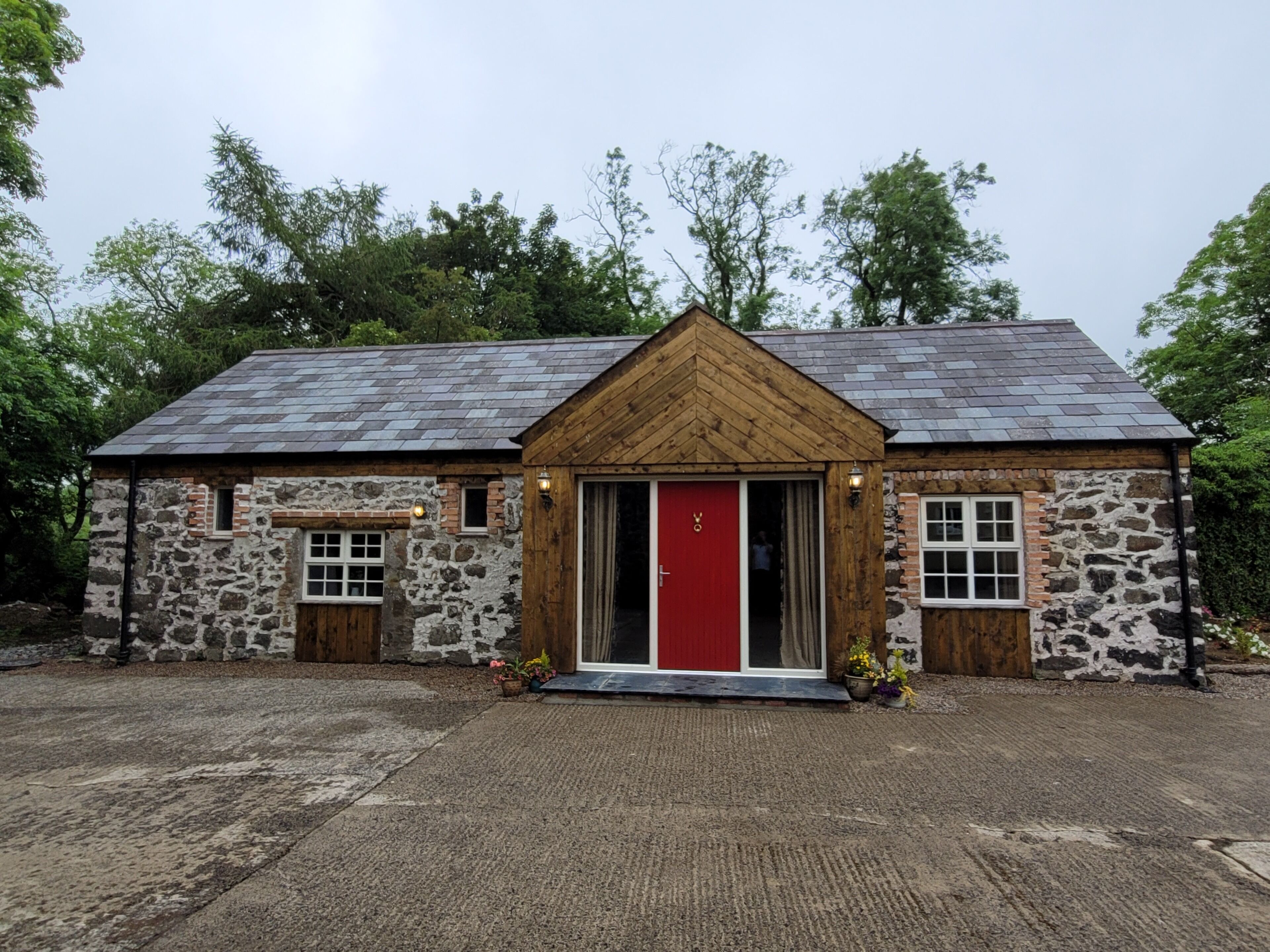 Un bâtiment en pierre avec une porte rouge, des éléments décoratifs en bois et une allée gravillonnée.