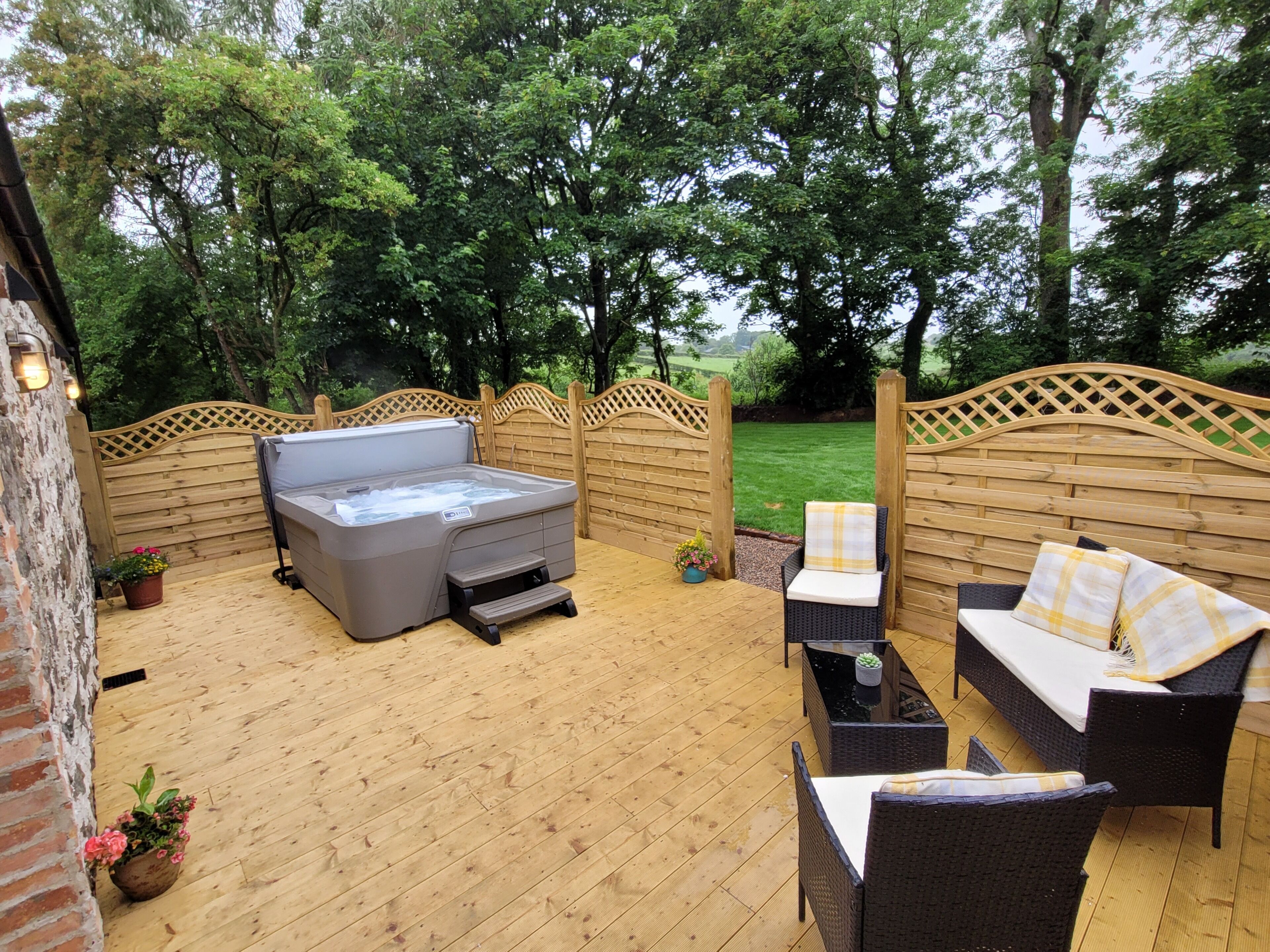 Un patio al aire libre con jacuzzi, mobiliario de mimbre y una valla de madera.