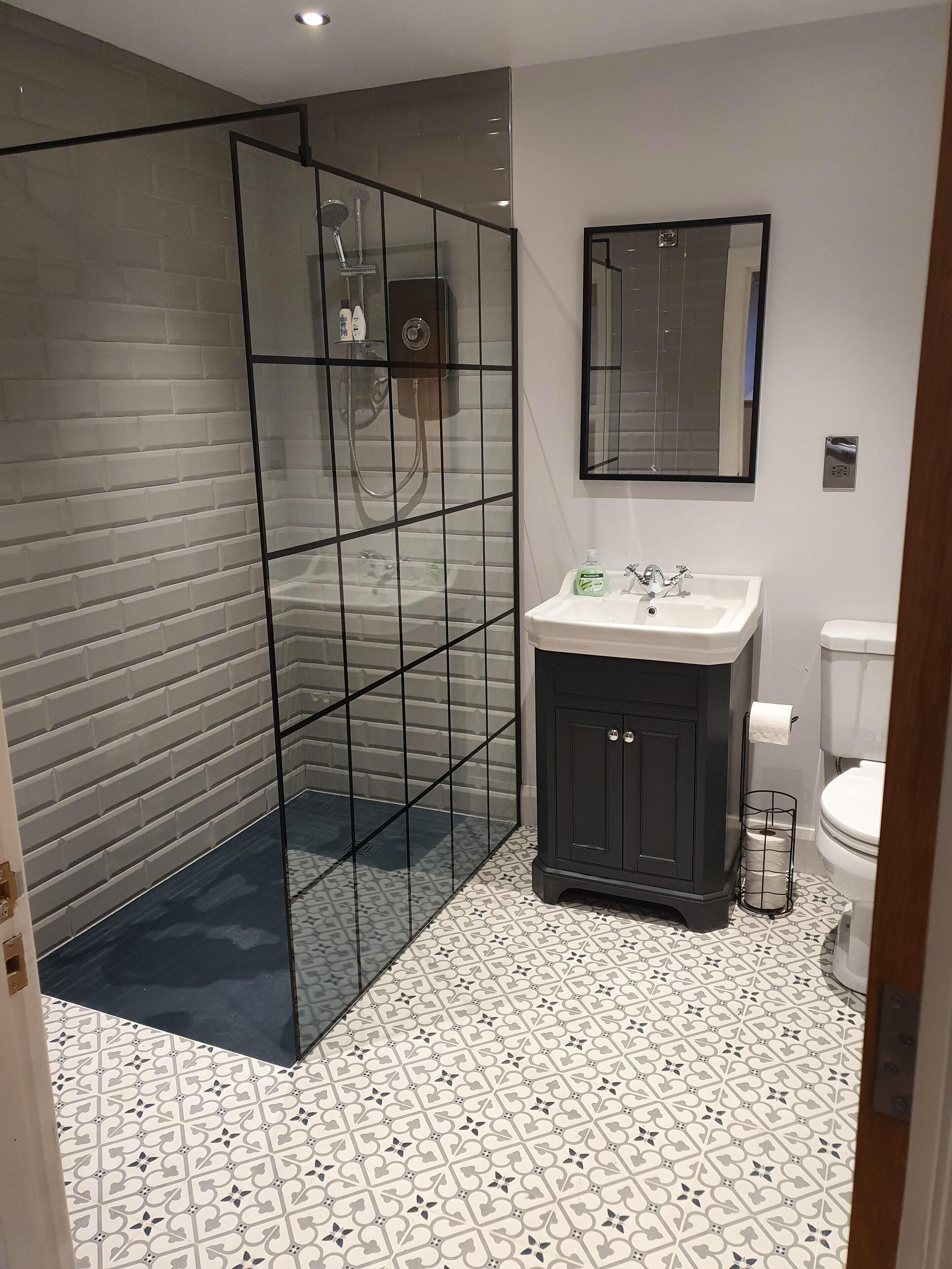A modern bathroom with a glass-enclosed shower, a white sink with a dark cabinet, and a toilet.