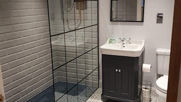 Ein modernes Badezimmer mit einer gläsernen Duschkabine, einem weißen Waschbecken mit dunklem Unterschrank und einer Toilette.