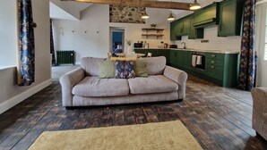 A modern living room with a sofa, wooden beams, a kitchen with green cabinets, and a dining area. - Hawthorn Hollow (Ballymena)