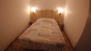 Een kleine, knusse kamer met een bed, een houten hoofdeinde en twee wandlampen.
