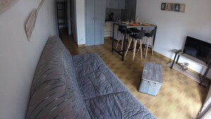 Een knus woongedeelte met een bank, een eethoek met stoelen, een televisie en een keuken op de achtergrond.