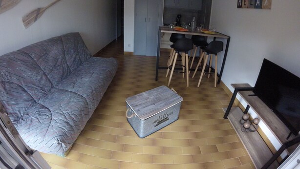 A compact living space with a sofa, a small table with chairs, a kitchen area, and a television.