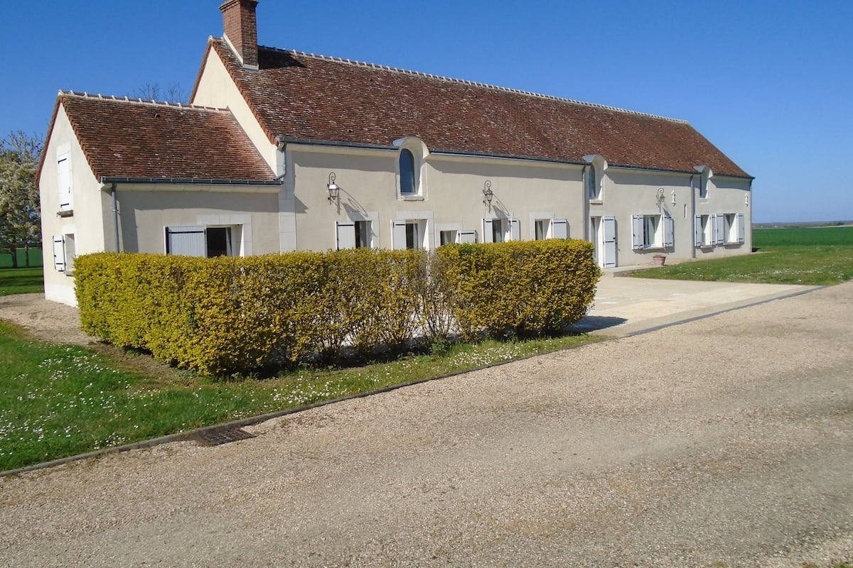 A large, single-story building with a tiled roof, a gravel driveway, and a well-maintained hedge in front.