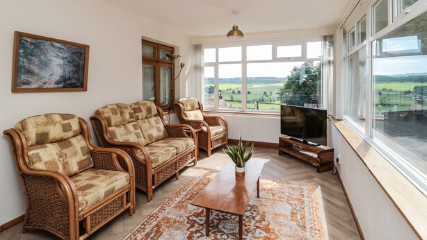 A living room with wicker furniture, a flat-screen TV, and a large window with a view of the countryside. - Rose Bank (Belford)