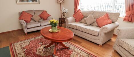 A living room with two sofas, a coffee table, a patterned rug, a framed picture on the wall, and a window with curtains.